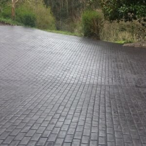 Entrada de garaje de una casa unifamiliar pavimentada con hormigón impreso gris textura adoquín y un coche aparcado.